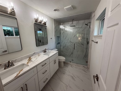Primary bathroom featuring a marble finish shower, a textured ceiling, double vanity, marble finish floors, and a textured wall