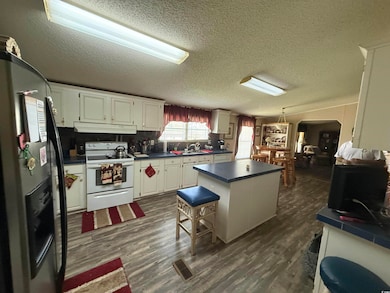 Kitchen featuring electric range, black refrigerator with ice dispenser, under cabinet range hood, a kitchen island, and dark countertops