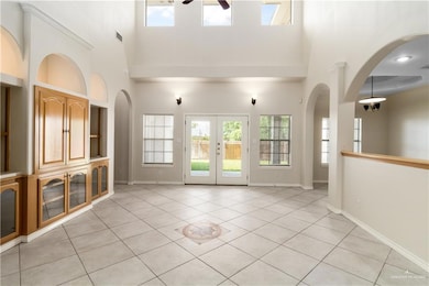 Unfurnished living room with a towering ceiling, ceiling fan, healthy amount of natural light, light tile patterned flooring, and arched walkways