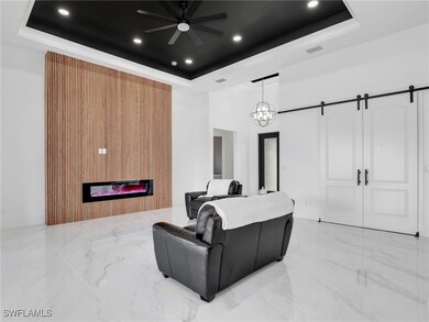 Cinema room with a barn door, a glass covered fireplace, a raised ceiling, light marble finish floors, and recessed lighting