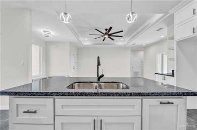 Kitchen featuring a ceiling fan, white cabinets, recessed lighting, dark stone counters, and a tray ceiling