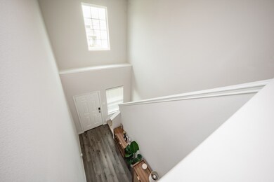 This is a bright, airy staircase with modern grey flooring, white walls, and a high window providing natural light. The space is clean and minimalistic, with a small decorative area by the entrance door.