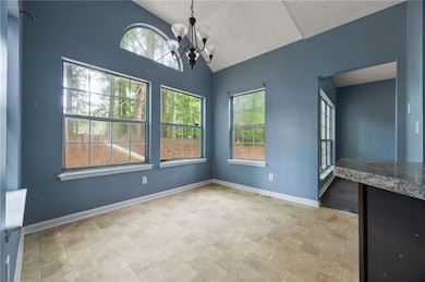 Unfurnished dining area with plenty of natural light, a chandelier, vaulted ceiling, and baseboards