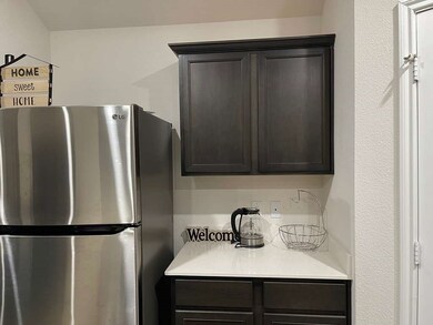 Kitchen with freestanding refrigerator, light stone countertops, and dark brown cabinetry
