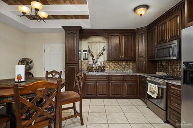 Kitchen with decorative backsplash, appliances with stainless steel finishes, dark brown cabinets, a chandelier, and stone counters