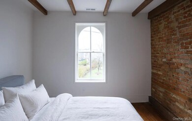 Bedroom featuring wood finished floors, brick wall, and beam ceiling