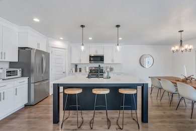 Kitchen with a kitchen island with sink, light wood finished floors, white cabinetry, a kitchen breakfast bar, and recessed lighting