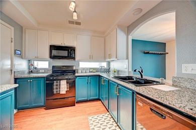 Kitchen featuring black appliances, blue cabinets, light wood finished floors, light stone countertops, and white cabinets