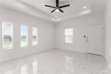 Empty room with a raised ceiling, ceiling fan, baseboards, and a wealth of natural light