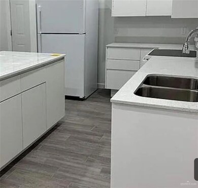 Kitchen with white cabinets, freestanding refrigerator, light wood-type flooring, and light stone countertops