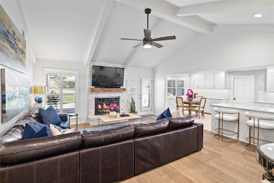 Living room with a fireplace, beam ceiling, light wood finished floors, high vaulted ceiling, and ceiling fan