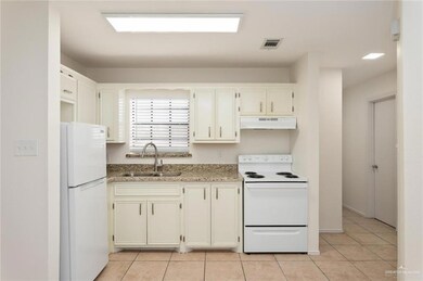 Kitchen with light tile patterned floors, white appliances, light stone counters, and sink