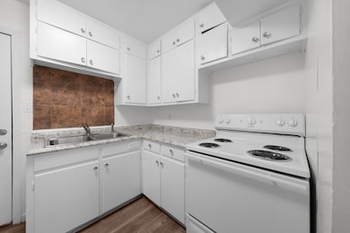 Kitchen featuring electric stove, white cabinetry, light countertops, and dark wood-style floors