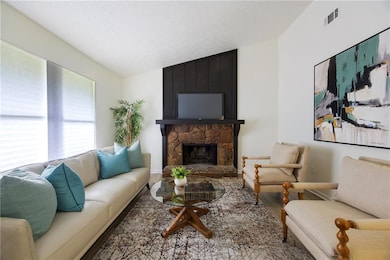 Living room with wood finished floors, a stone fireplace, and lofted ceiling