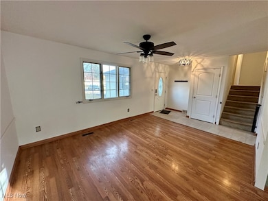 Entry with stairs, light wood-type flooring, a chandelier, and ceiling fan