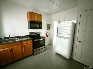 Kitchen with brown cabinetry, electric stove, dark countertops, and black microwave