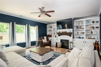 Living room featuring a ceiling fan, ornamental molding, wood finished floors, and a glass covered fireplace