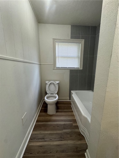 Bathroom with toilet, wood finished floors, a tub