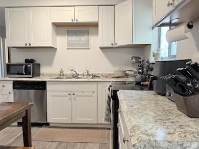 Kitchen with stainless steel appliances, light countertops, white cabinets, a textured wall, and light wood-style flooring