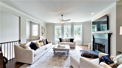 Living area with a ceiling fan, ornamental molding, wood finished floors, and a fireplace with flush hearth