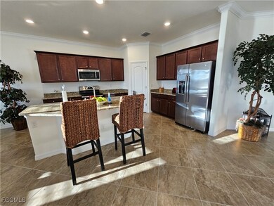 Kitchen featuring tile flooring, stainless steel appliances, light stone counters, and a center island with sink