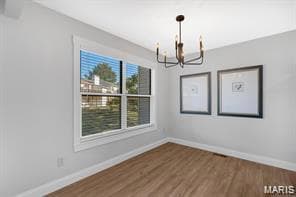 Unfurnished dining area featuring wood finished floors and a chandelier
