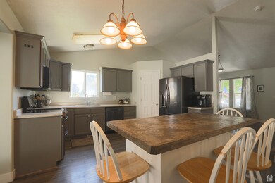 Kitchen featuring pendant lighting, black appliances, dark wood-type flooring, gray cabinets, and a chandelier