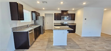 Kitchen with dark brown cabinets, recessed lighting, stainless steel appliances, light wood finished floors, and light stone countertops