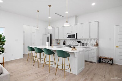 Kitchen featuring tasteful backsplash, stainless steel appliances, a center island with sink, decorative light fixtures, and light wood-type flooring
