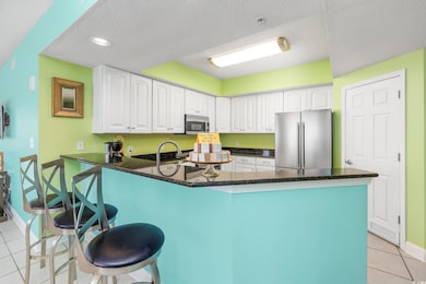 Kitchen with stainless steel appliances, a peninsula, light tile patterned floors, white cabinetry, and a breakfast bar area