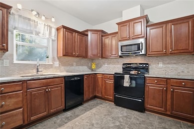 Kitchen featuring tasteful backsplash, black appliances, light stone counters, and brown cabinets