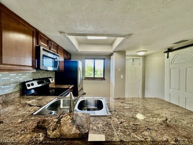 Kitchen featuring a barn door, a textured ceiling, stainless steel appliances, a raised ceiling, and dark stone counters