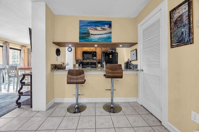 Kitchen with black appliances, light tile patterned floors, a peninsula, a breakfast bar area, and backsplash