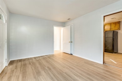 Unfurnished bedroom with freestanding refrigerator and light wood finished floors