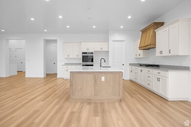 Kitchen featuring recessed lighting, an island with sink, light wood finished floors, and white cabinets