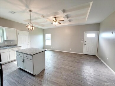 Kitchen with coffered ceiling, white cabinetry, ceiling fan, hanging light fixtures, and light stone countertops