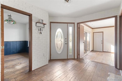 Entrance foyer featuring wood finished floors, brick wall, and ornamental molding