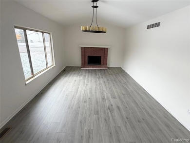 Unfurnished living room with a brick fireplace, vaulted ceiling, and light wood-style floors