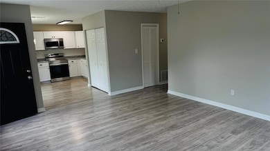 Kitchen with backsplash, appliances with stainless steel finishes, open floor plan, light wood-style floors, and white cabinetry