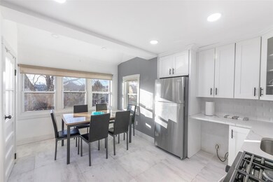 Kitchen with white cabinetry, backsplash, freestanding refrigerator, light stone countertops, and glass insert cabinets