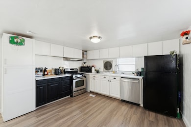 Kitchen with white cabinetry, black appliances, light wood-style flooring, and light countertops