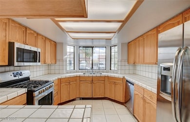Kitchen with appliances with stainless steel finishes, tile countertops, light tile patterned floors, and decorative backsplash