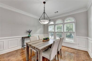 Dining space featuring a decorative wall, wainscoting, crown molding, and light wood finished floors
