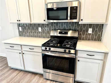 Kitchen with stainless steel appliances, light wood-style flooring, white cabinets, and tasteful backsplash
