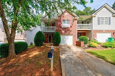 View of front of house featuring brick siding, a balcony, an attached garage, and driveway
