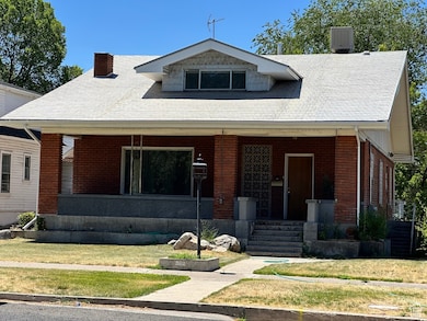 Bungalow-style home with a porch, brick siding, a front yard, and a chimney