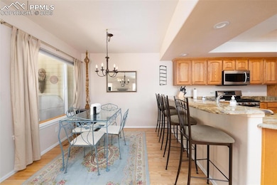 Kitchen featuring appliances with stainless steel finishes, a breakfast bar area, light stone counters, light wood finished floors, and a chandelier