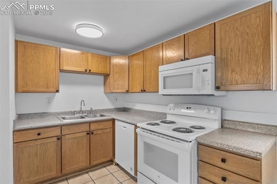 Kitchen featuring white appliances, brown cabinets, light countertops, and light tile patterned floors