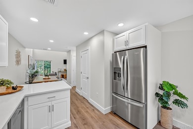Kitchen featuring light countertops, stainless steel fridge, white cabinets, recessed lighting, and light wood-style flooring