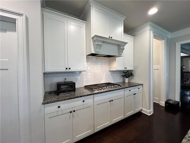 Kitchen with stainless steel gas cooktop, under cabinet range hood, baseboards, tasteful backsplash, and crown molding